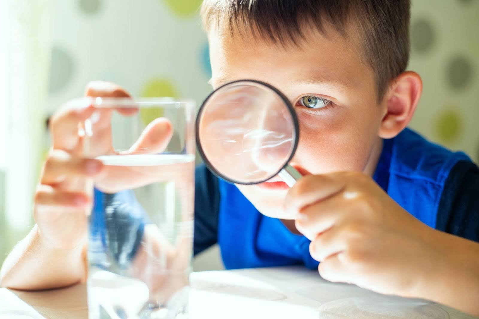 A little boy looking at a glass of water with a magnifying glass