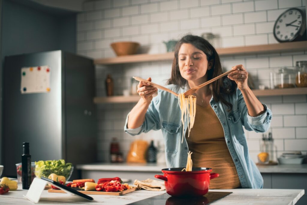 Pregnant woman smelling the pasta dish she's cooking on the stovetop