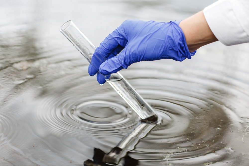 Scientist's hand gathering a test tube full of water from a pond or lake or ocean