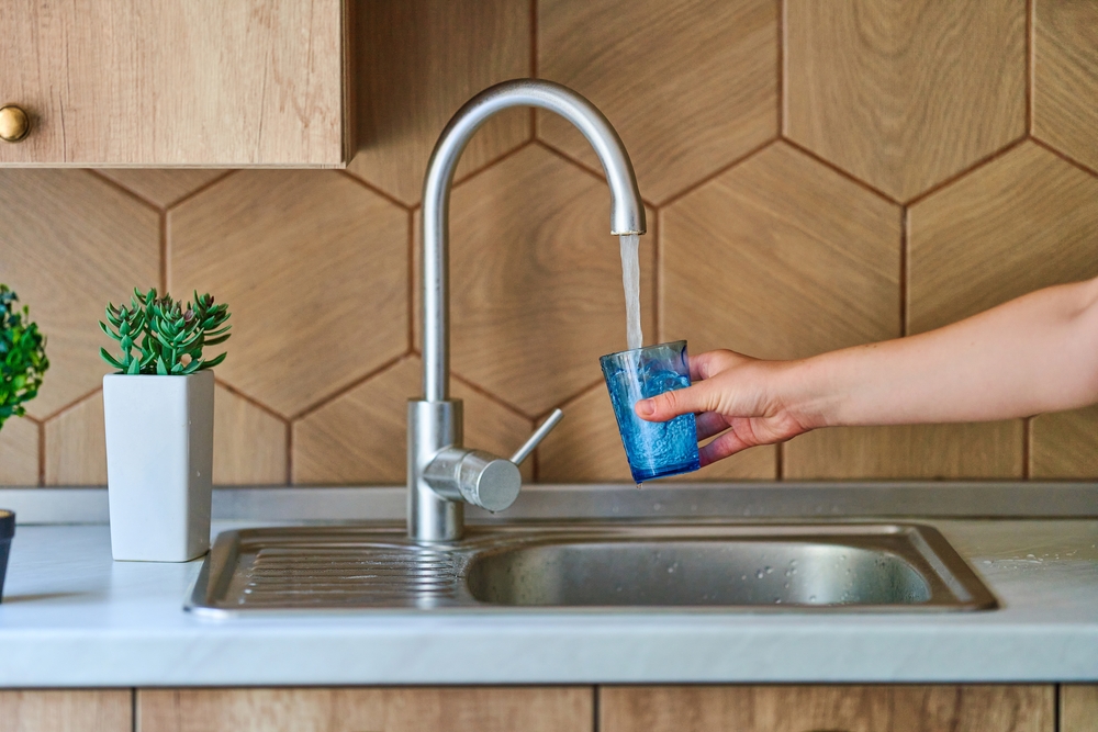Female hand filling a blue cup with water from the kitchen sink