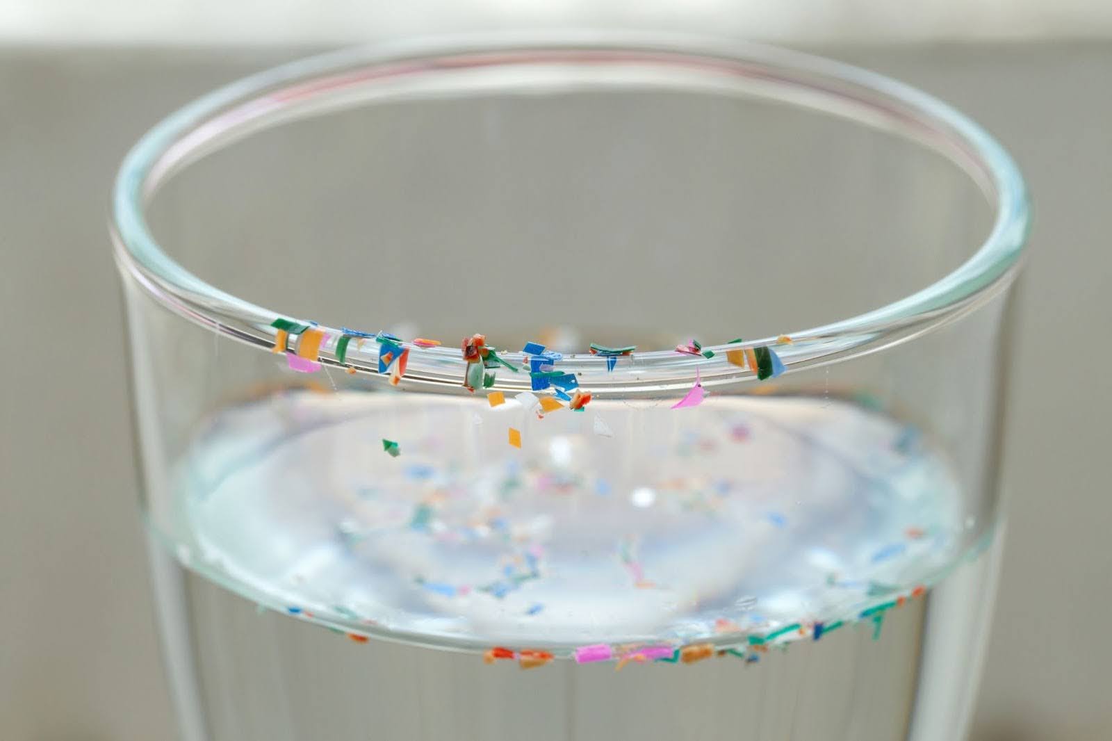 A glass of water with colorful plastic pieces floating in it to represent microplastics in drinking water