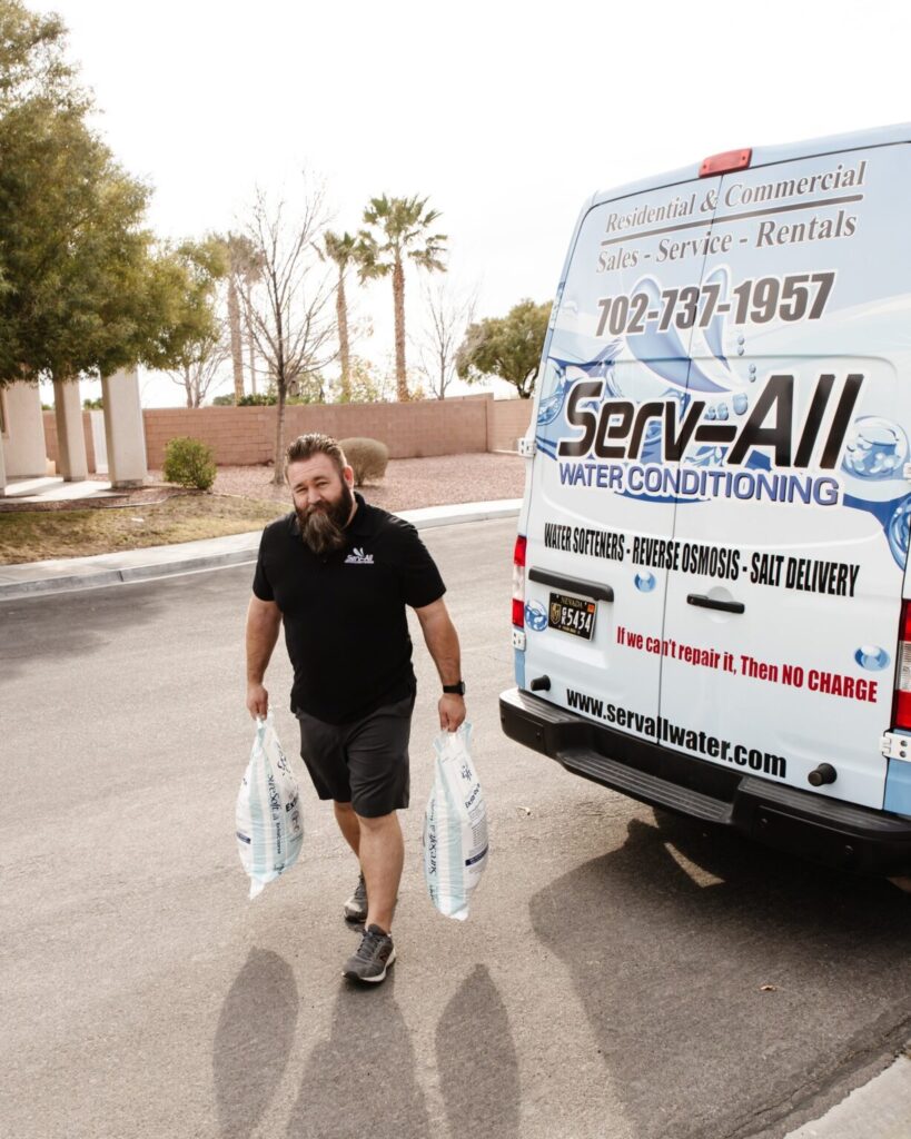 owner of Serv-All Water Conditioning carrying two bags of water softener salt while standing next to a Serv-All van