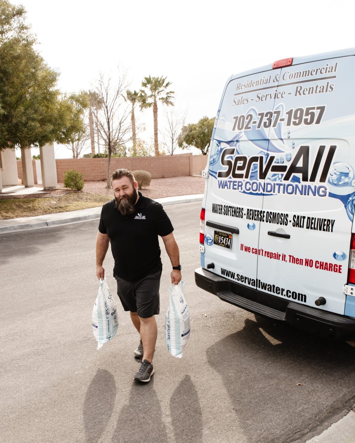 owner of Serv-All Water Conditioning carrying two bags of water softener salt while standing next to a Serv-All van