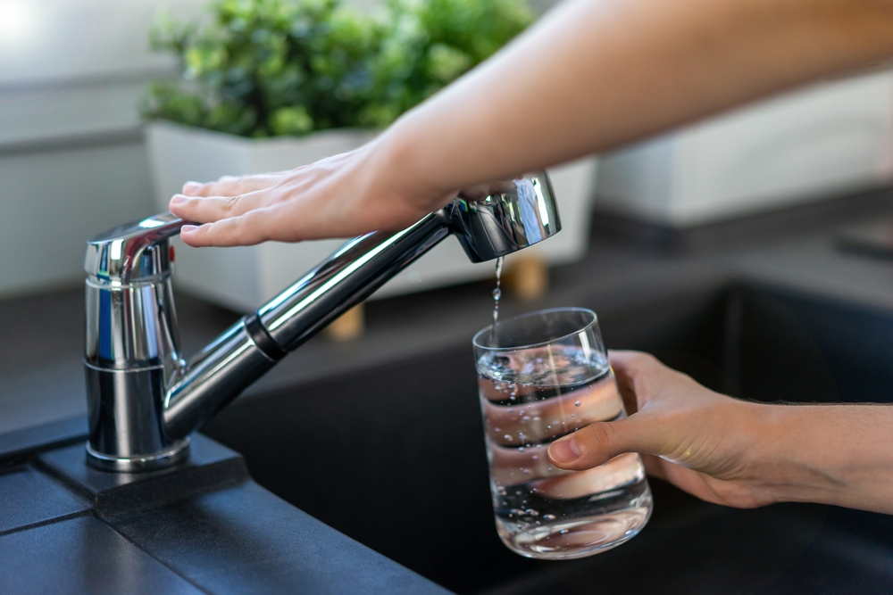 a woman's hands using the kitchen sink faucet to get a glass of tap water